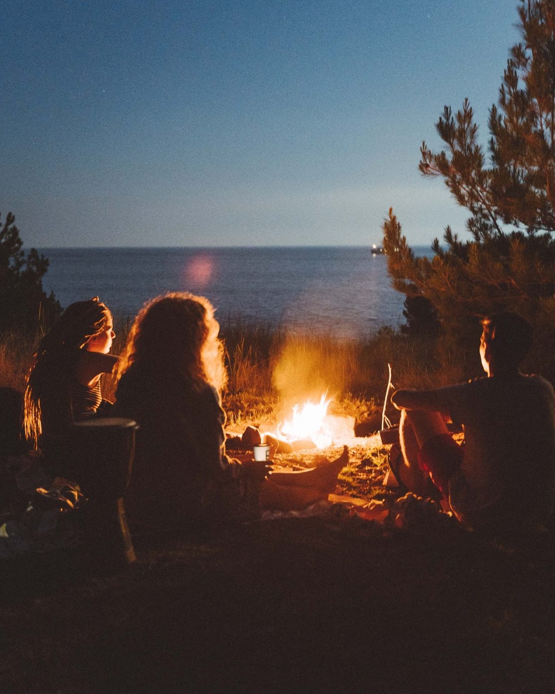 Friends around a campfire by the sea at dusk